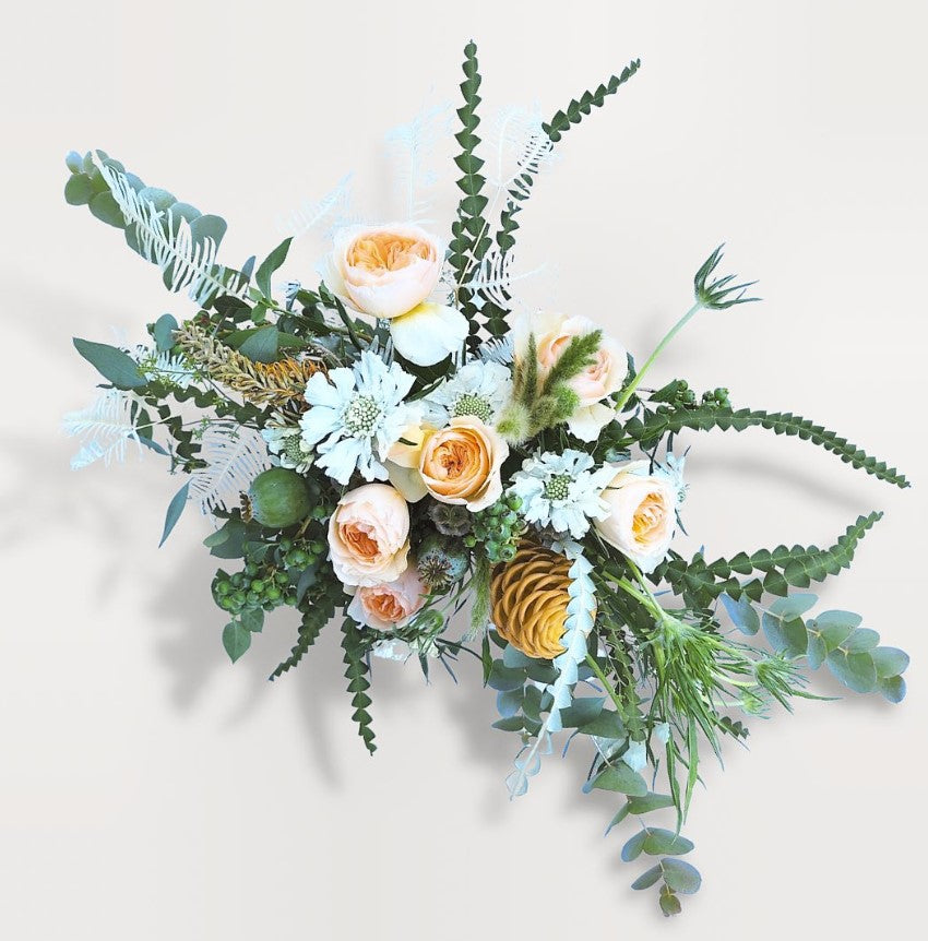 Page Elliott Floral Subscription in "Standard" size. Overhead shot shows white scabiosa, peach garden roses, banksia protea foliage, blueberries, eucalyptus and grevellia.  